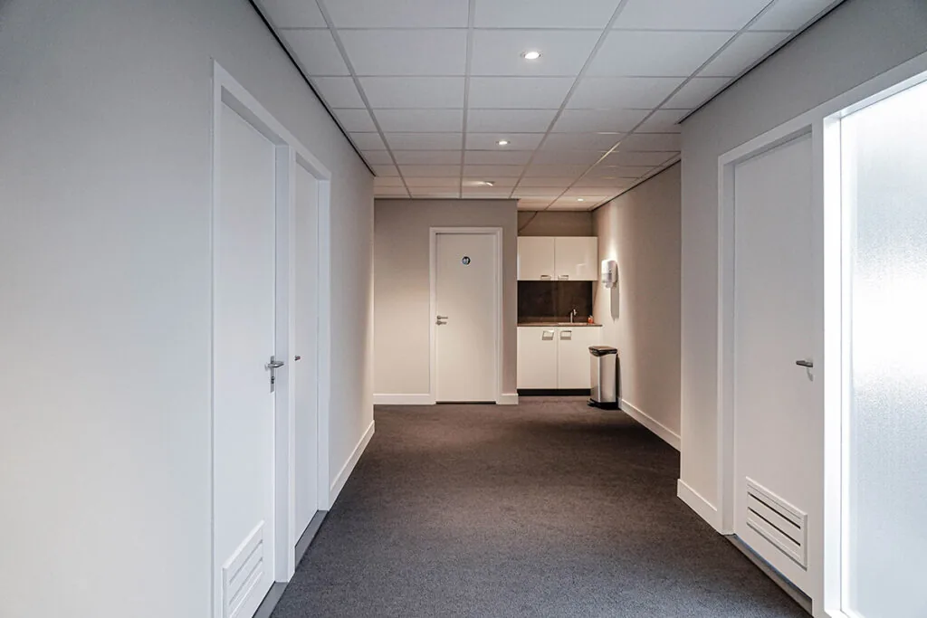 Gang in een kantoorpand aan de Burgemeester van Karnebeeklaan met meerdere deuren en een kitchenette achterin.